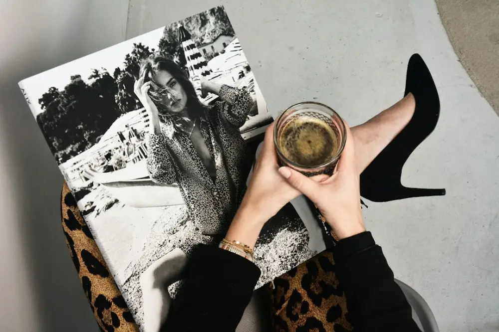 A person holding a glass of coffee over a black and white fashion magazine, illustrating reading fashion imagery thoughtfully